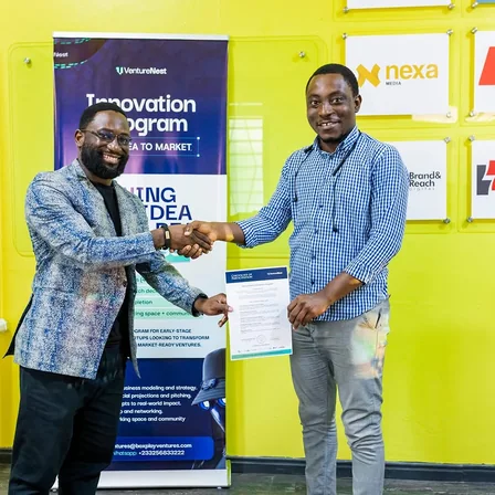 Two founders shaking hands in front of the Venture Nest Innovation Program banner.